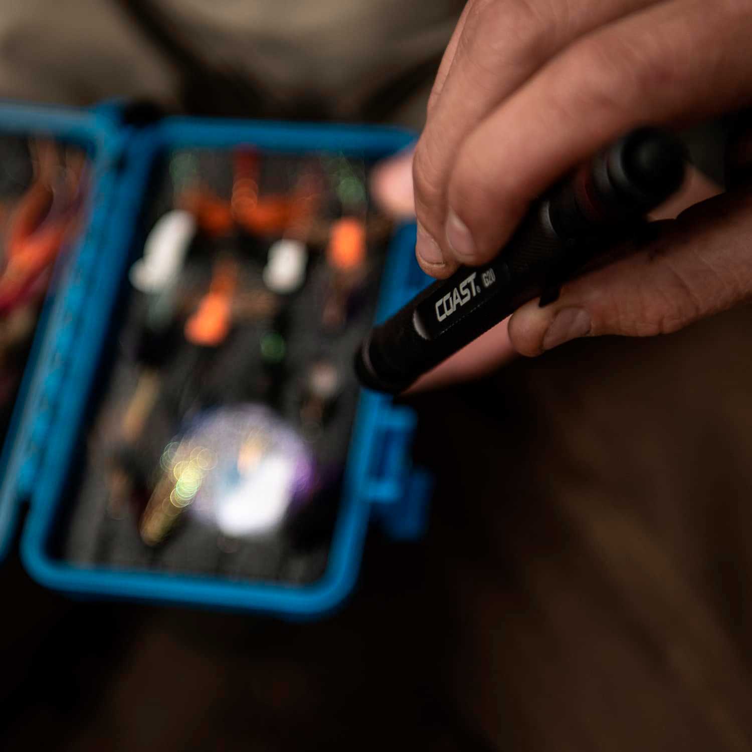 écnico utilizando la LINTERNA  G20 mientras inspecciona herramientas dentro de una caja metálica, enfocando el haz de luz uniforme iluminando llaves y desarmadores.